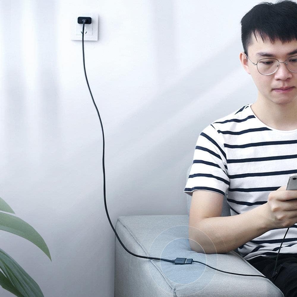 Person sitting on a couch using a smartphone with a cable plugged into an outlet.